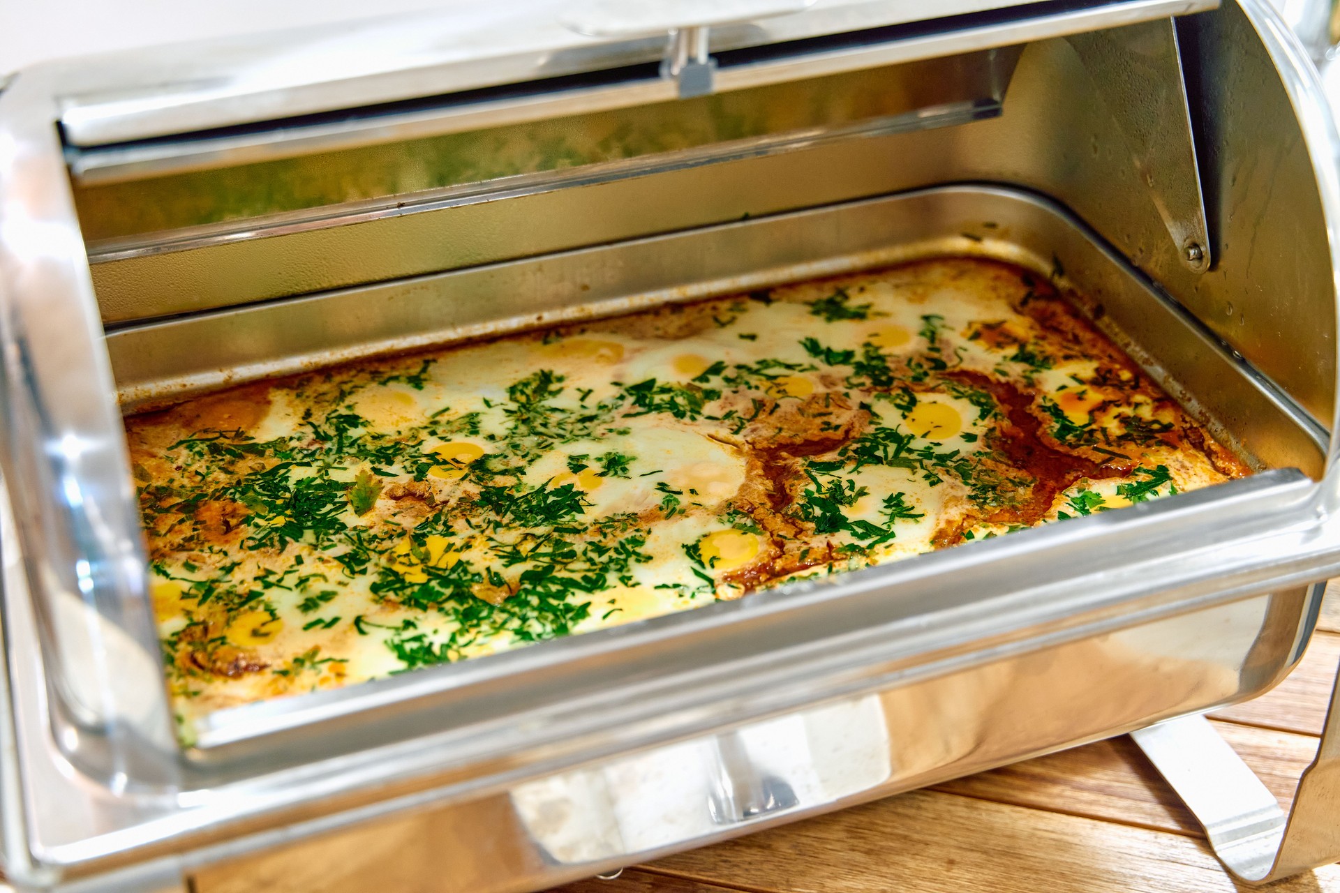 A beautifully cooked dish served in a gleaming chafing dish with fresh herbs and spices, showcasing a tantalizing brown crust and appealing presentation.